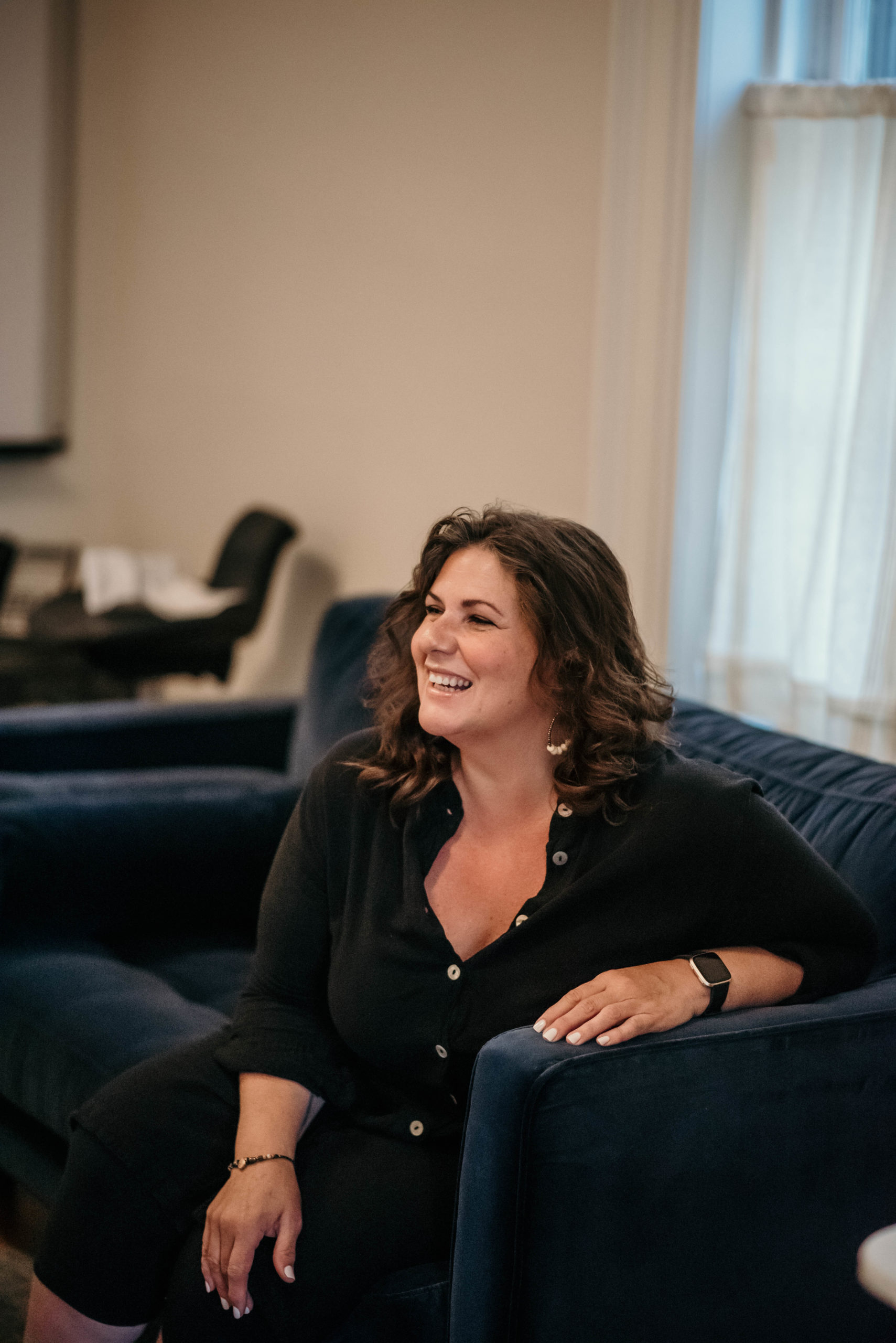 Photo of Josie Grant sitting on dark blue couch, looking away from the camera, and smiling.