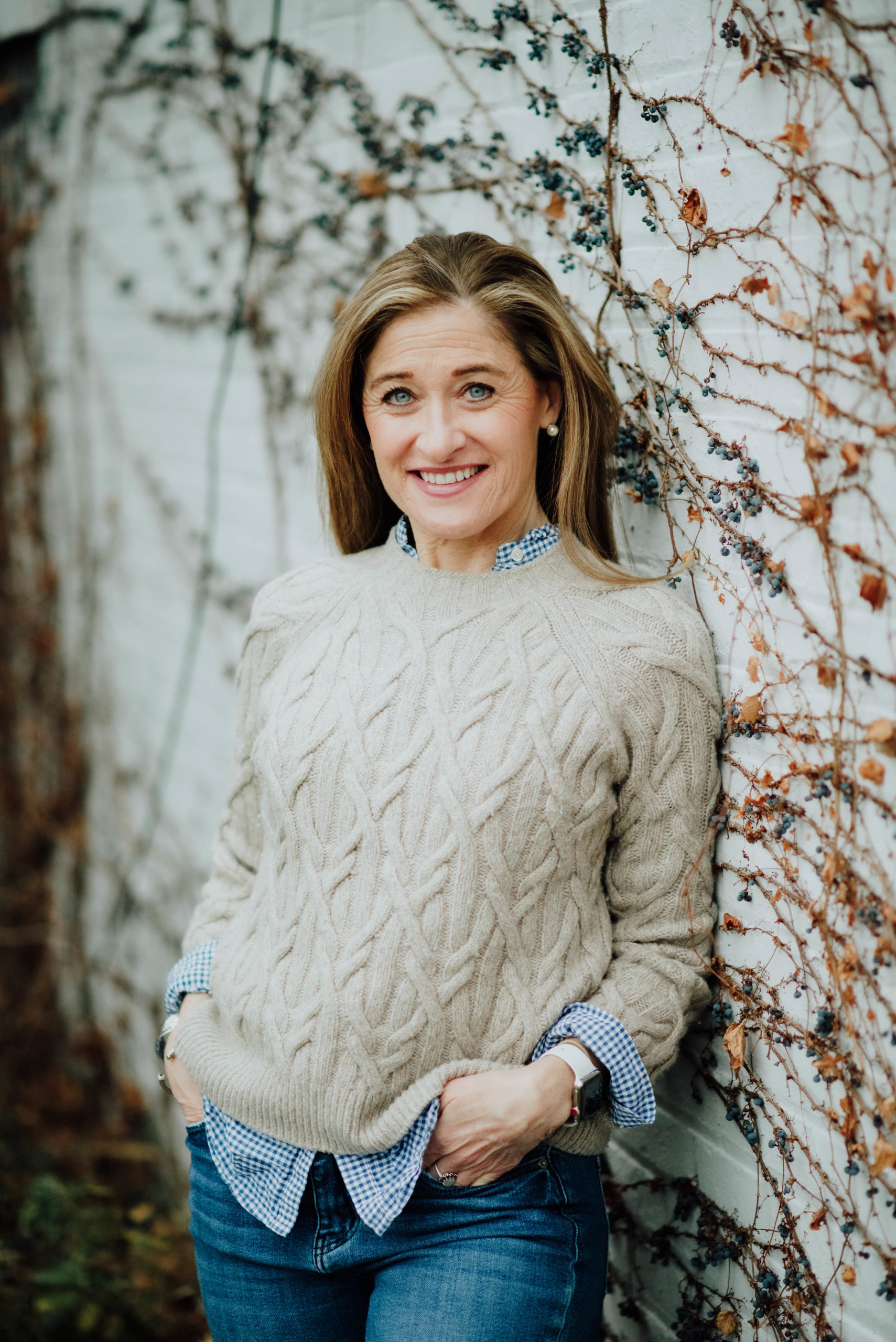 Photo of Anne Kenney, the head of marketing at Hale Advisors, outside with her hands in her front pockets and leaning back onto a wall with vines